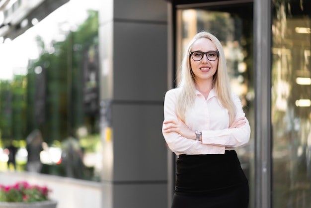 Hermosa mujer de negocios con una falda negra de camisa y gafas posando Sonriendo y mirando la cámara frente a la entrada del centro de negocios