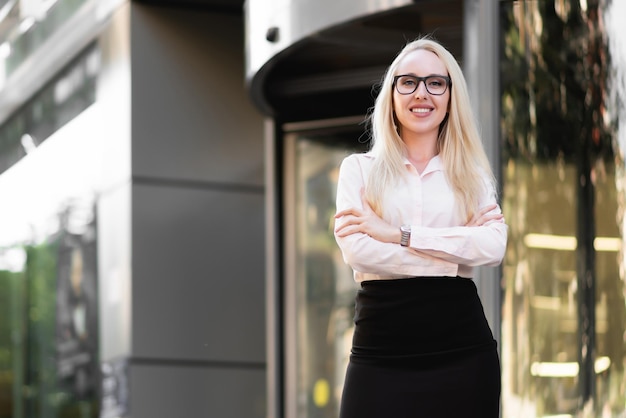Hermosa mujer de negocios con una falda negra de camisa y gafas posando Sonriendo y mirando la cámara frente a la entrada del centro de negocios