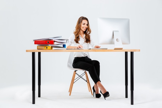 Foto hermosa mujer de negocios feliz usando la computadora mientras está sentado en el escritorio en la oficina isoltaed sobre el fondo blanco.