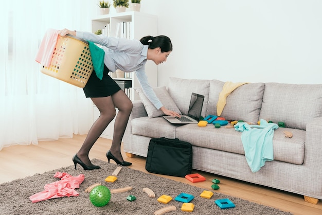 hermosa mujer de negocios japonesa está usando un cuaderno para responder el correo electrónico y limpiar los juguetes y la ropa desordenados en casa.