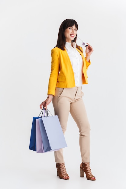 hermosa mujer de negocios joven feliz posando aislada sobre pared blanca sosteniendo bolsas de la compra.