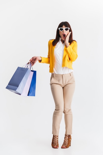 hermosa mujer de negocios joven sorprendida posando aislada sobre pared blanca con bolsas de la compra.