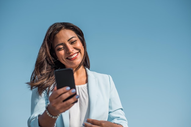 Hermosa mujer de negocios latina feliz escribiendo o leyendo mensajes sms en línea en un teléfono inteligente Copiar espacio