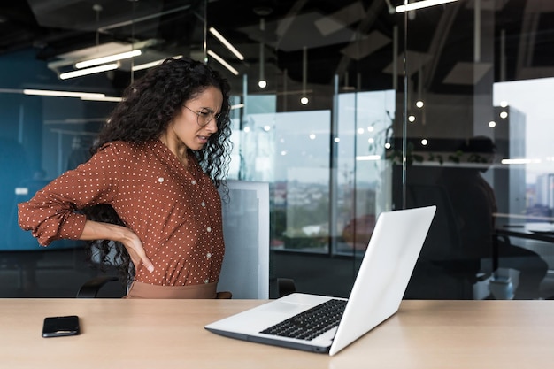 Hermosa mujer de negocios latinoamericana que trabaja en una oficina moderna cansada tiene una espalda severa