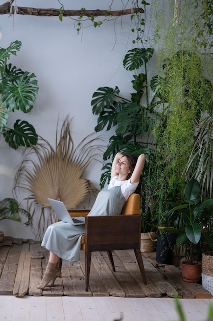 Hermosa mujer de negocios con las manos detrás de la cabeza y la computadora relajándose soñando despierta en las plantas circundantes