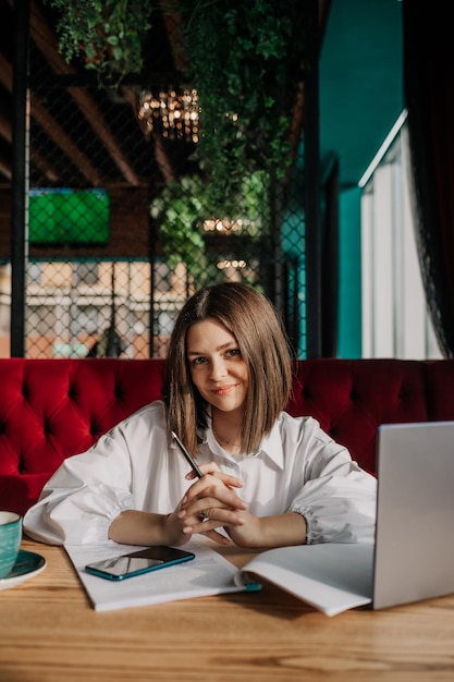 Una hermosa mujer de negocios morena con una camisa blanca está sentada en una mesa en un café con una computadora portátil