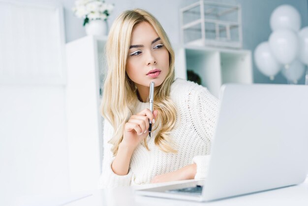 Hermosa mujer de negocios pensativa que trabaja con una laptop en una oficina moderna