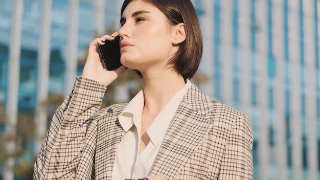 Hermosa mujer de negocios que parece confiada hablando por teléfono mientras espera un taxi en el centro. Señora elegante en la calle de la ciudad