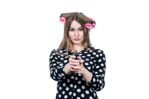 hermosa mujer de negocios en rulos apuntando con un arma a la cámara aislada en un fondo blanco