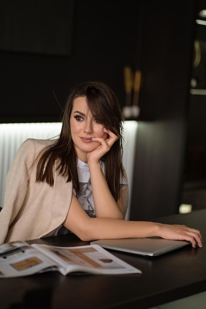 Foto una hermosa mujer de negocios está sentada en una mesa en su oficina laptop y revistas en la mesa