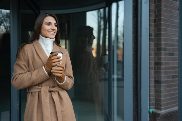 Hermosa mujer de negocios con una taza de café cerca de la entrada del edificio de oficinas