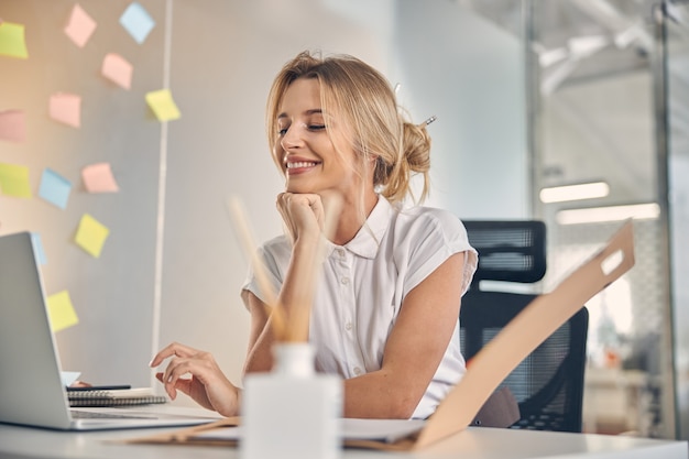 Hermosa mujer de negocios trabajando en un cuaderno y sonriendo mientras está sentado en la mesa en la oficina