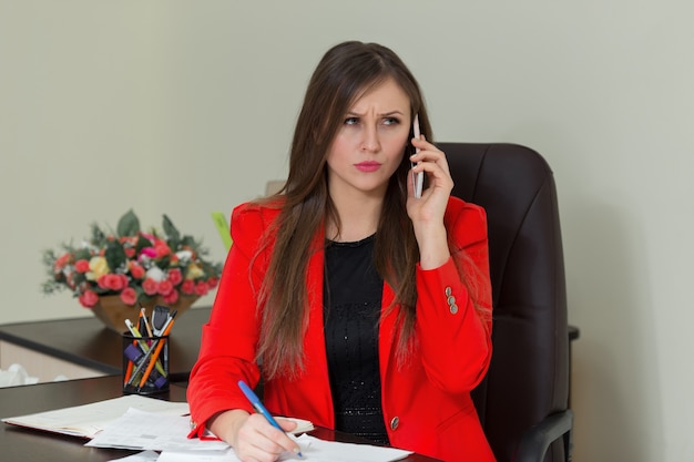 Hermosa mujer de negocios trabajando en su escritorio de oficina con documentos y hablando por teléfono.