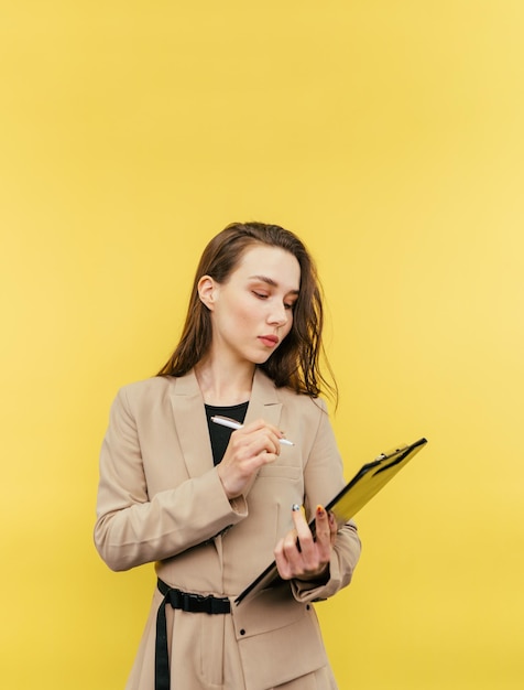 Hermosa mujer de negocios con traje beige se para con una tableta de papel en la mano