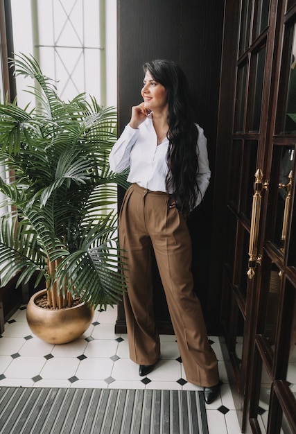 Hermosa mujer de negocios con traje de negocios posando cerca de una puerta de vidrio