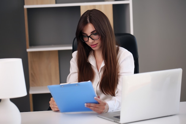 Hermosa mujer de negocios usa una computadora portátil y sonríe mientras trabaja en la oficina