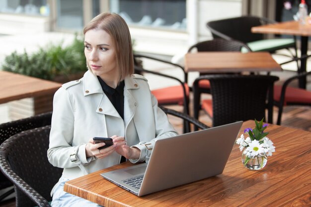 Hermosa mujer de negocios usando un teléfono inteligente y una computadora portátil en un café al aire libre