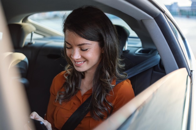 Foto hermosa mujer de negocios está usando un teléfono inteligente y sonriendo mientras está sentada en el asiento trasero del auto mujer usando un teléfono inteligente y sonriendo mientras está sentada en el asiento trasero del auto