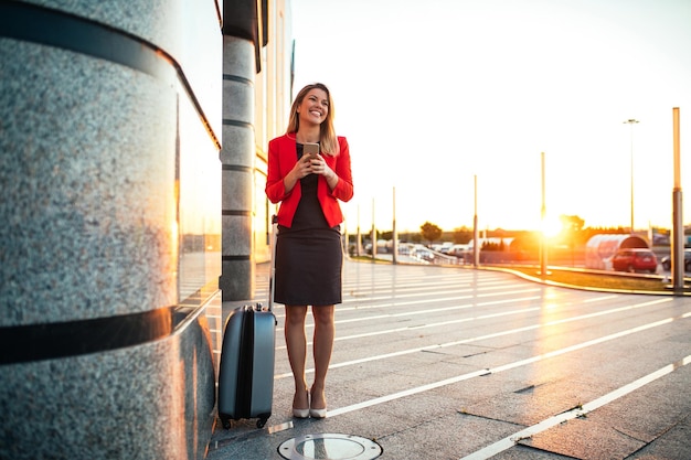 Hermosa mujer de negocios usando teléfono móvil mientras está de pie en un aeropuerto