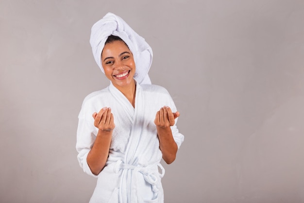 Hermosa mujer negra brasileña con albornoz y toalla invitando a llamar con las manos