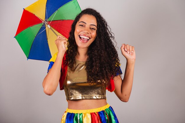 Hermosa mujer negra brasileña con traje de frevo y paraguas carnaval signo de paz y amor con los dedos