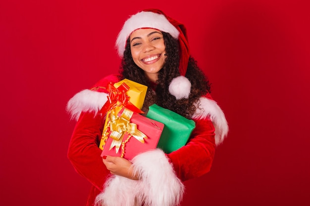 Hermosa mujer negra brasileña vestida como ropa de navidad de santa claus con tres regalos