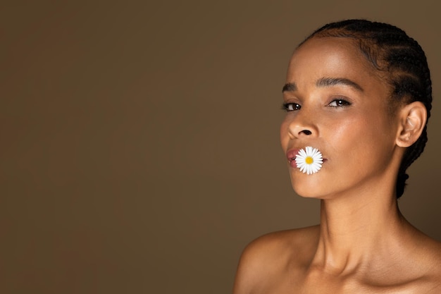 Hermosa mujer negra de mediana edad con piel brillante posando con una linda flor blanca de manzanilla en ella