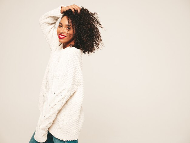 Hermosa mujer negra con peinado de rizos afro y labios rojos. Modelo sonriente en ropa de jeans de moda y suéter de invierno.