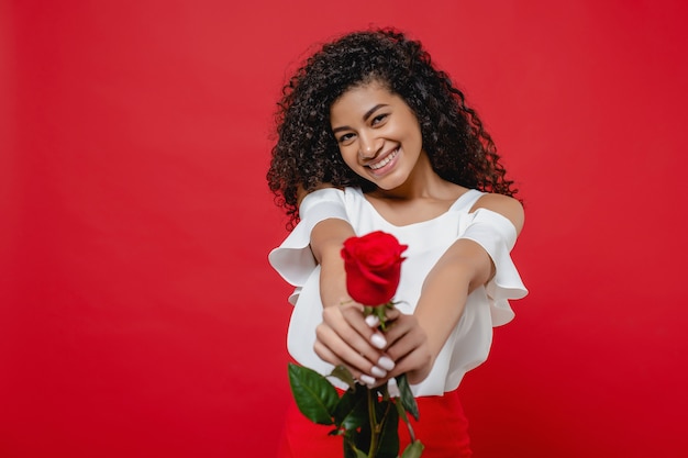 Hermosa mujer negra con rosa en manos aisladas sobre rojo