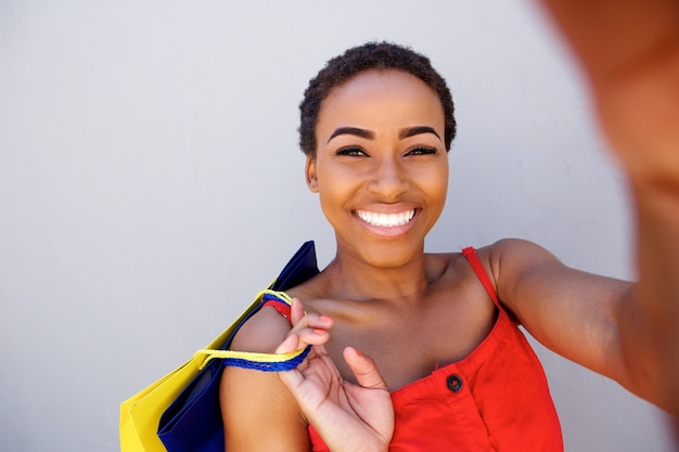 Hermosa mujer negra sonriendo con bolsas de compras tomando un selfie