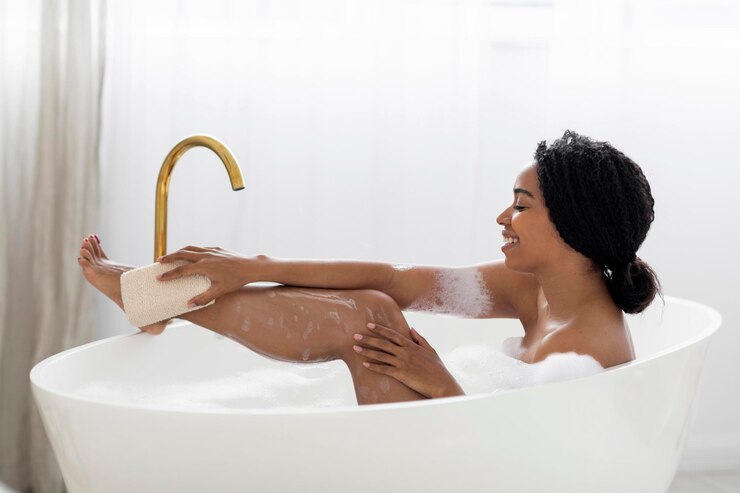 Hermosa mujer negra tomando un baño espumoso y usando una esponja corporal
