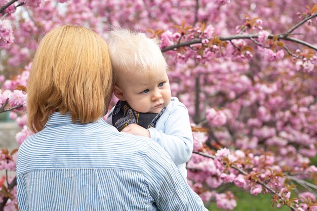 Hermosa mujer con un niño pequeño cerca de un árbol floreciente de sakura rosa Concepto de primavera