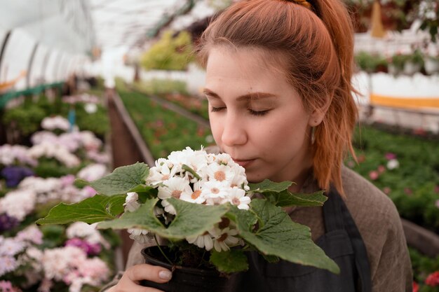 Hermosa mujer con los ojos cerrados inhala el aroma del crisantemo en el invernadero del centro comercial jardín