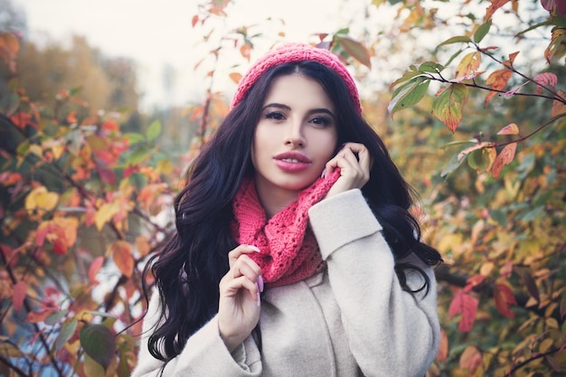 Hermosa mujer de otoño con el pelo largo y oscuro sosteniendo la hoja de arce roja al aire libre