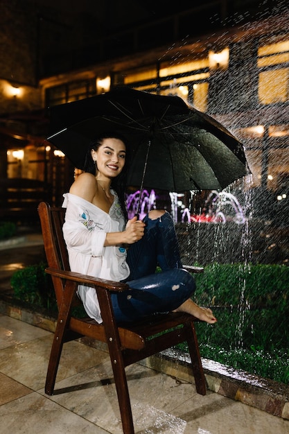 Hermosa mujer con el paraguas sentado en el banco