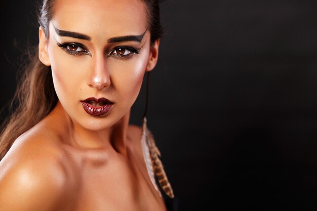 Foto hermosa mujer parece un sagitario con maquillaje oscuro y plumas en los oídos