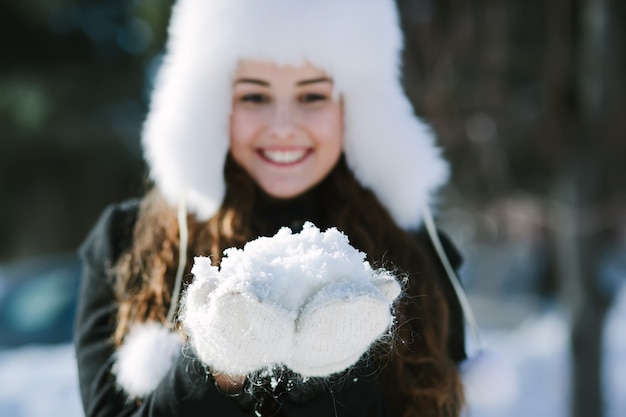 Hermosa mujer en el parque de invierno con un puñado de nieve