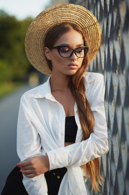 Hermosa mujer pasea por la calle con gafas y un sombrero