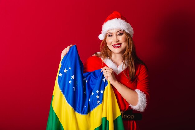 Foto hermosa mujer pelirroja brasileña vestida con ropa de navidad santa claus sosteniendo la bandera de brasil