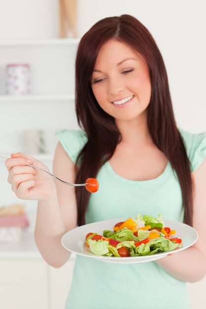 Hermosa mujer pelirroja disfrutando de una ensalada mixta en la cocina