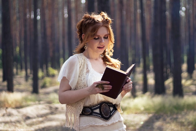 Hermosa mujer pelirroja lee un libro en el bosque, imagen vintage