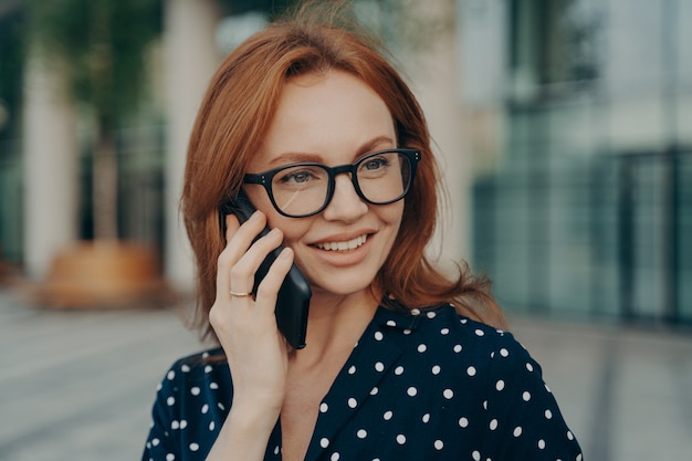 Hermosa mujer pelirroja tiene conversación telefónica usa teléfono inteligente para llamar