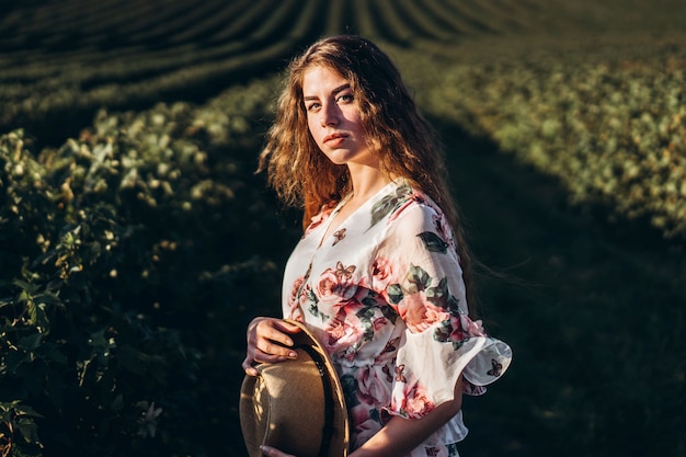 Hermosa mujer con pelo largo y rizado y cara de pecas en campo de grosella. mujer en un vestido ligero camina en el día soleado de verano