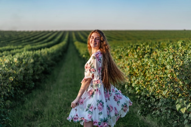 Hermosa mujer con pelo largo y rizado y cara de pecas en campo de grosella. mujer en un vestido ligero camina en el día soleado de verano