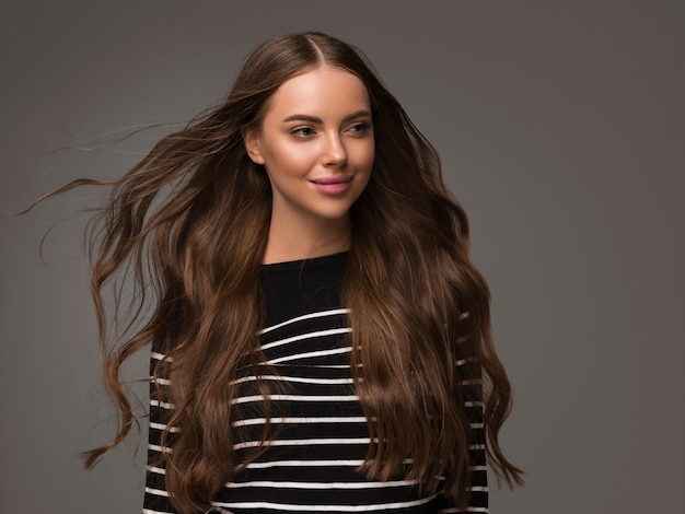 Hermosa mujer con pelo rizado largo sano en suéter de rayas casual. Fondo de color.