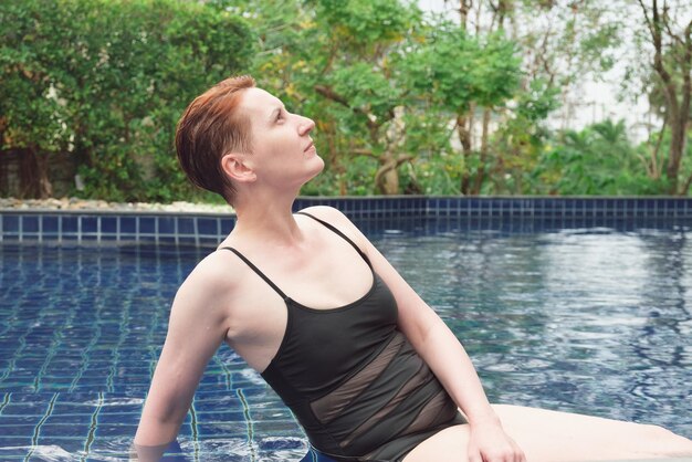 Hermosa mujer con el pelo rojo corto se relaja en la piscina