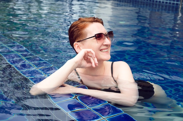 Hermosa mujer con el pelo rojo corto se relaja en la piscina