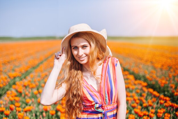 Hermosa mujer de pelo rojo con vestido a rayas de pie en coloridos campos de flores de tulipanes