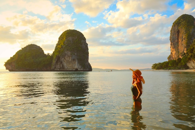 Hermosa mujer de pie en el agua durante la puesta de sol en la playa tropical de Railay Krabi Tailandia