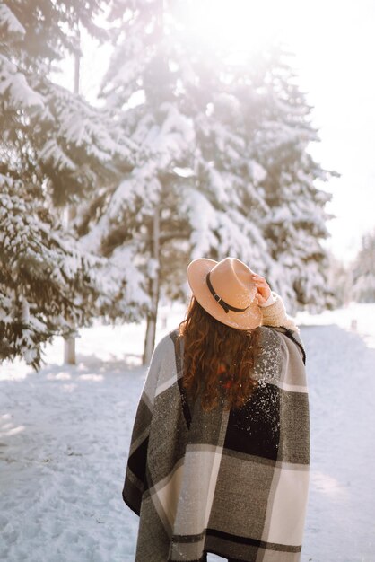 Hermosa mujer de pie entre árboles nevados y disfrutando de la primera nieve. Momento feliz. Navidad.